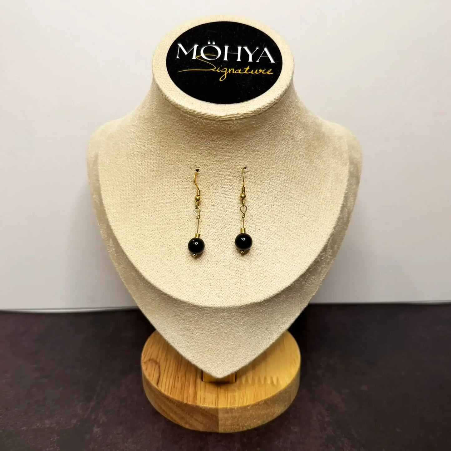 Brincos pendentes dourados com pedra ônix preta em expositor de joias elegante.