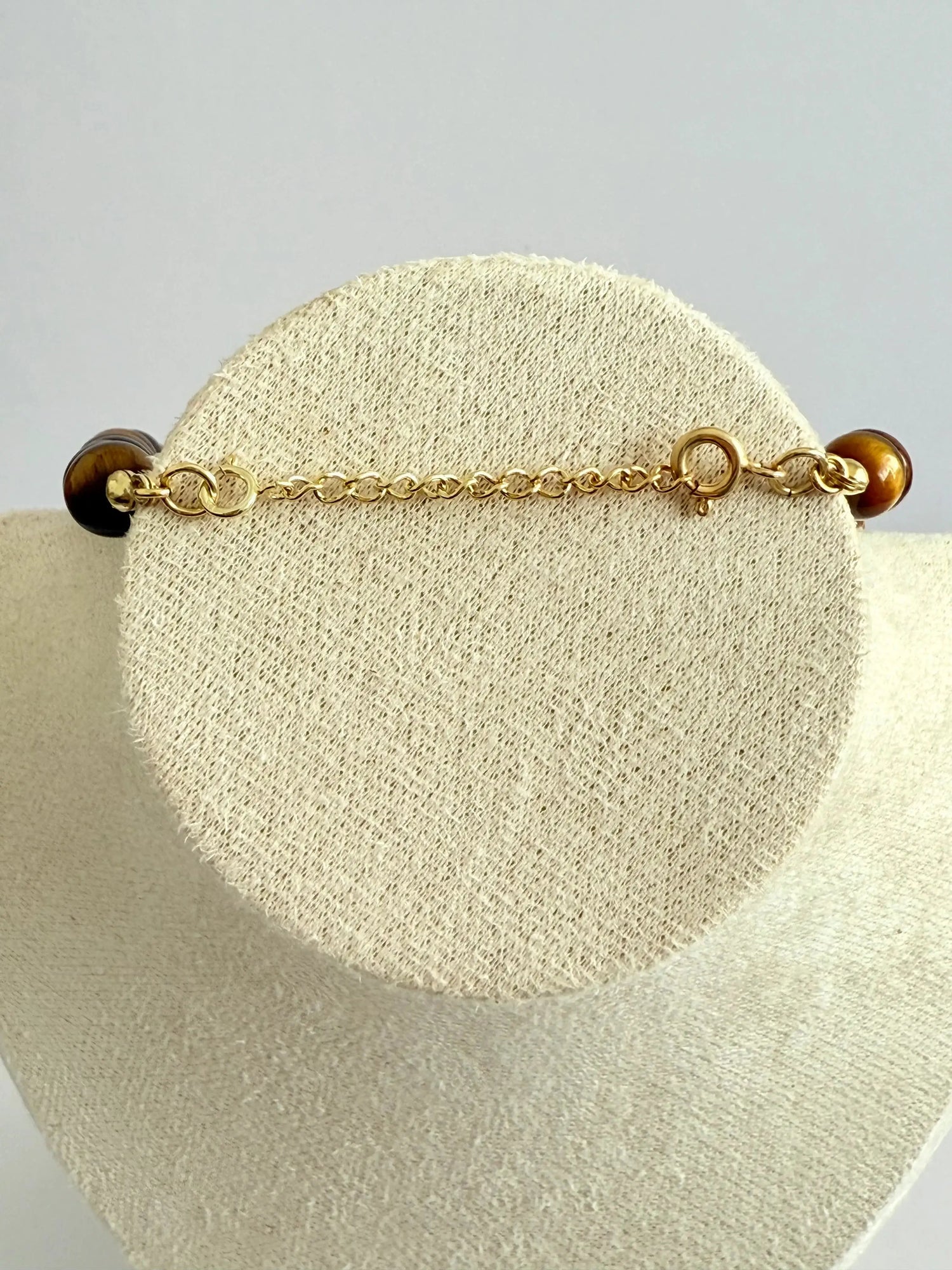 Pulseira de prata banhada a ouro com fecho e pedra natural, exibida em suporte claro.
