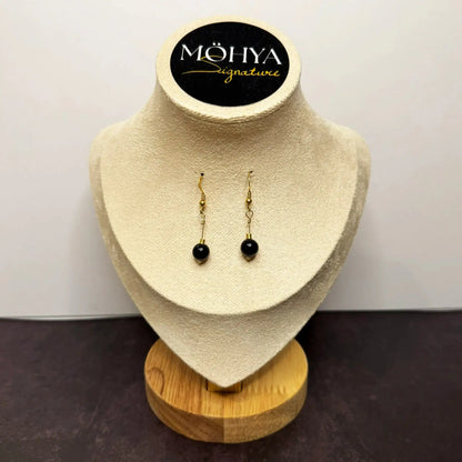 Brincos pendentes dourados com pedra ônix preta em expositor de joias elegante.