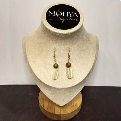Brincos pendentes de madrepérola e esfera dourada, expostos em suporte elegante.