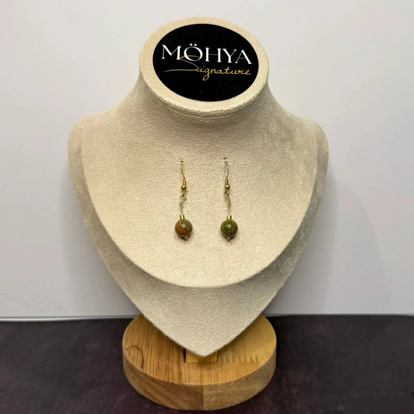 Brincos de prata com pedra unakita esverdeada, exposição em suporte de veludo bege.