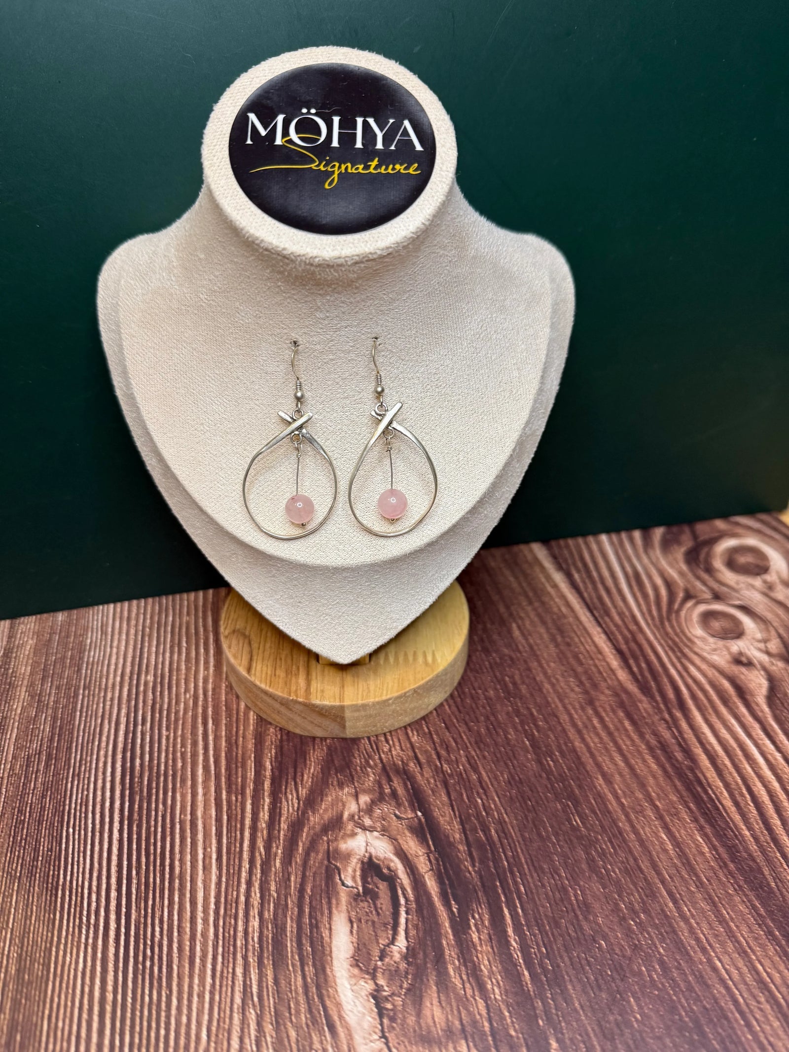 Par de brincos de prata com pedra rosa, design artesanal, expostos em suporte de veludo bege.