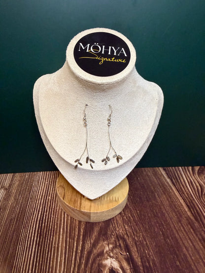 Brincos pendentes de prata 925 com design delicado, expostos em suporte de joias.