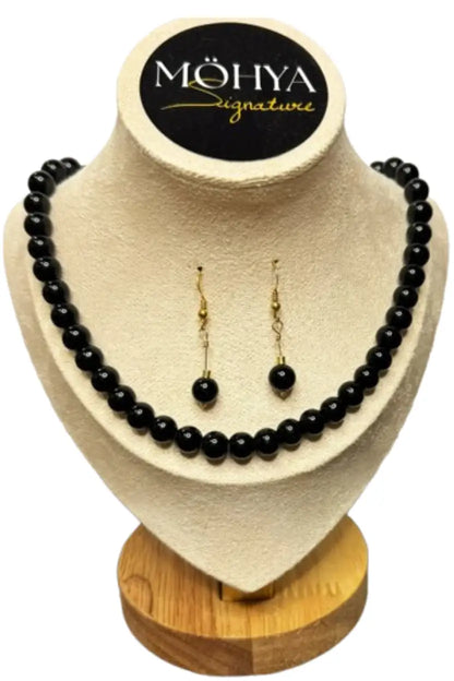 Conjunto de colar e brincos de contas pretas, exposto em suporte bege com base de madeira.